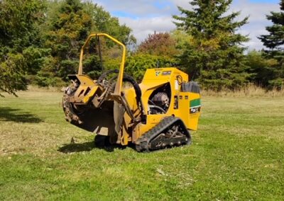 Yellow trencher on grassy field with trees.